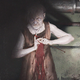 An old woman with white eyes crochets menacingly in a dingy sewer.